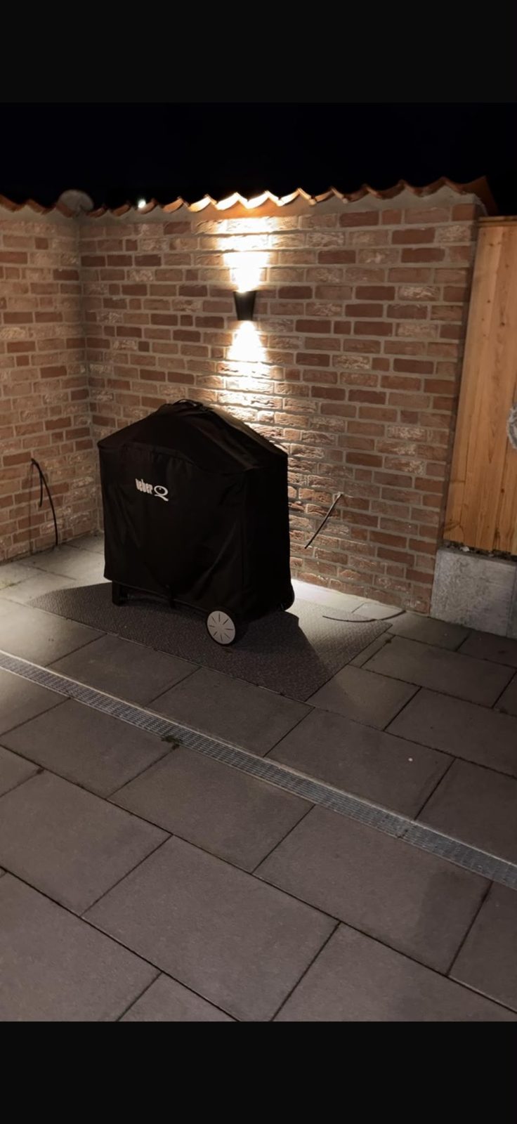 Außenanlage / Grillplatz – Ergebnis: gemauerte Klinkerwand mit Beleuchtung und gepflastertem Grillplatz bei Abendlicht